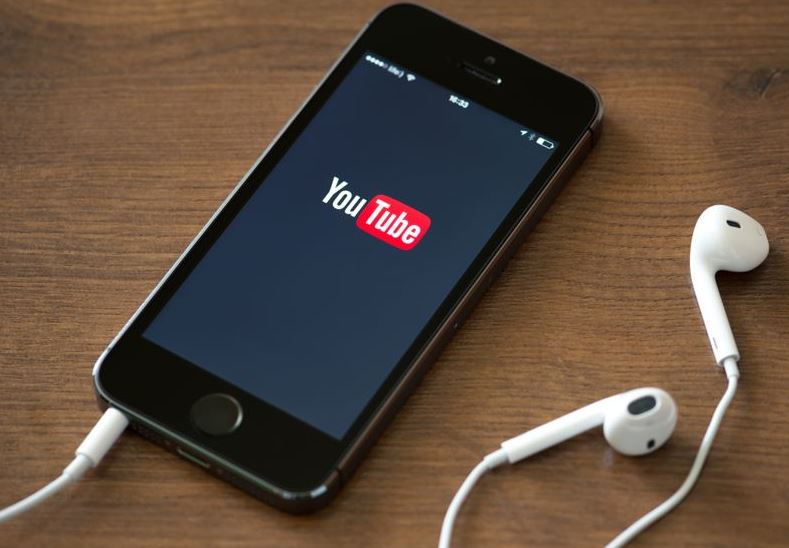 Kiev, Ukraine - June 5, 2014 Brand new Apple iPhone 5S with YouTube application service on the screen lying on a desk with headphones.