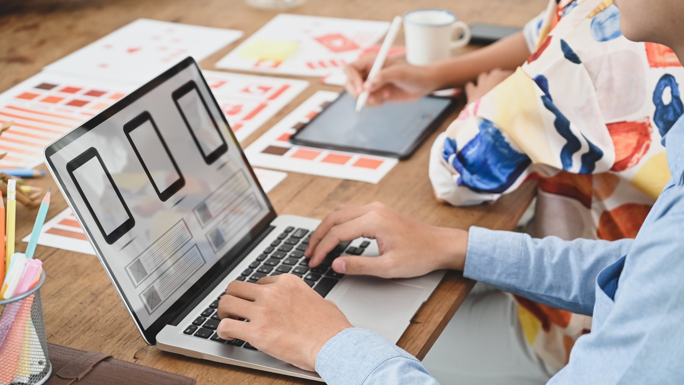 Cropped image of two people is using a computer laptop with an interface icon on the screen at the wooden table.