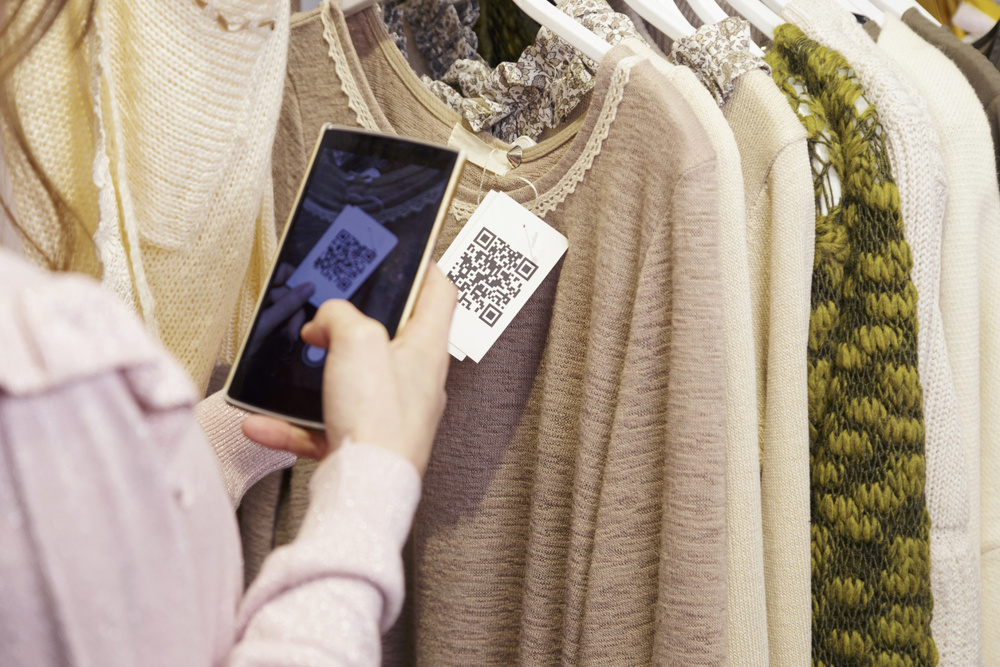 Woman scanning a QR code, with her smart phone, from a label in a clothing store. No face