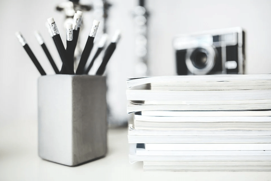 a stack of notebooks, pencils, pencil holder, camera